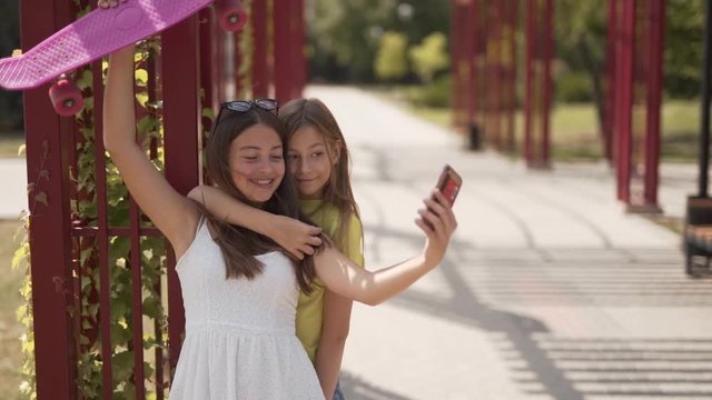 Two girlfriends taking pictures of themselves in a park with a phone