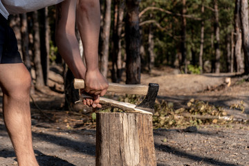 A man chopping wood on a stump in the forest on a sunny summer day. 