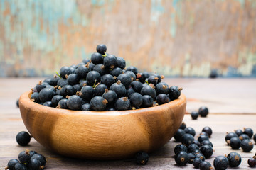 Ripe black currants in a wooden bowl on a wooden table