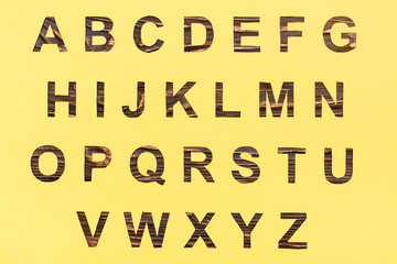 The letters of the English alphabet are cut out of yellow cardboard, a wooden background is visible in the gap.