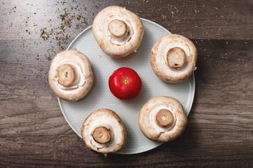 Closeup of white mushrooms with tomato on a white plate on a dark wooden table. Vegetarian healthy food