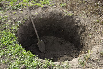 Deep pit in the ground. In the pit lies a shovel. Digging a hole. - obrazy, fototapety, plakaty