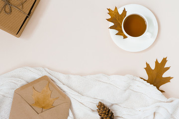 beautiful autumn composition with a Cup of tea. autumn leaves, Kraft gift box, an envelope and a knitted blanket on a beige background. the concept of the fall season. copy space. Autumn flat lay