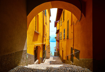 Varenna, Italy. Vintage narrow street of old Mediterranean town at lake Como in Lombardy region. Motley walls of houses and arch between buildings. Sunny summer day.
