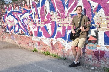 handsome bright guy with a guitar on the street against the background of a painted wall