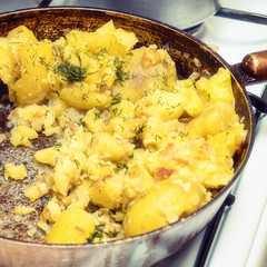 Fried potatoes with dill in a pan on a gas stove close up. Selective focus