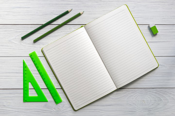 Blank open notebook and green stationery on a gray wood table. Ruler, eraser, pencil. Top view.