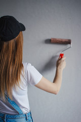 Selective focus at painting roller in young Caucasian woman hand in front of a reparing new wall in a room.