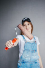 Selective focus at painting roller in young Caucasian woman hand in front of a reparing new wall in a room.