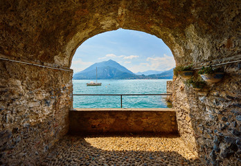 Varenna, Italy. View at lake Como with mountains and sailer yacht from stone arch at seafront.