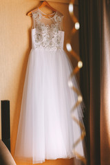 The perfect wedding dress with a full skirt on a hanger in the room of the bride