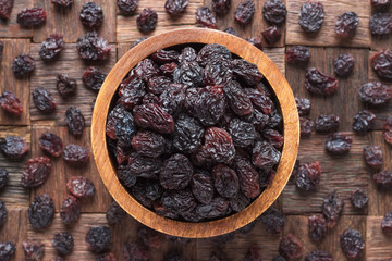 dried grapes, dark raisins in wooden bowl, top view.