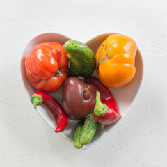 Ugly organic colorful tomato, pepper, cucumber in dish as heart. Concept organic vegetables.