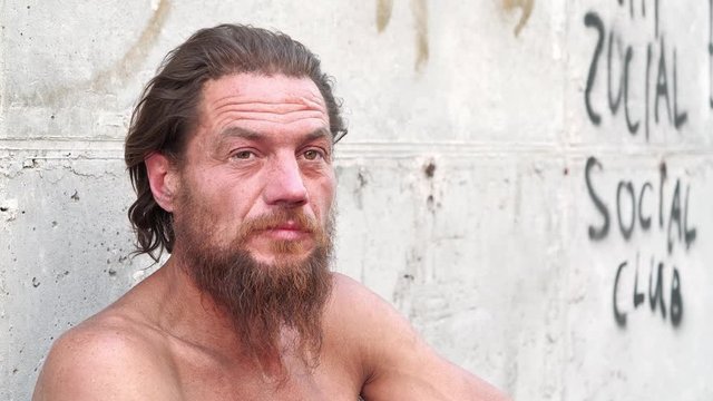 Down-and-out person on the street. Homeless man looks at the camera and talks. Real person with no fixed abode