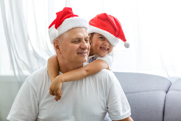 Obraz premium Close-up portrait of joyful girl hugging grandpa in headwear. grandfather and granddaughter in Santa Claus hats