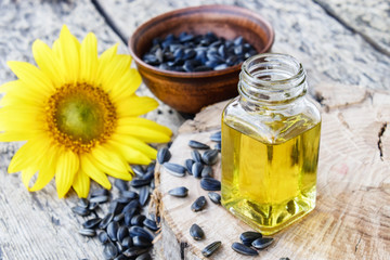 Sunflower oil and sunflower seeds in a bowl on a wooden background near fresh sunflower flowers. Organic and eco food.