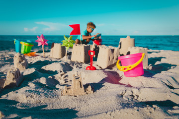 sand castle with toys and boy building it, kids play with sand