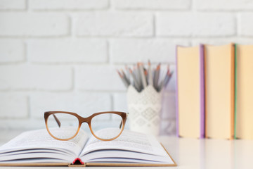 open book and glasses, pencils for drawing on the desktop against a white brick wall with a place for text. September 1st, back to school. horizontal frame