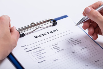 Close-up Of Human Hand Holding Pen Over Medical Report
