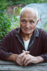 Close-up portrait of a very old man with arms crossed, sitting at a table on a blurred background...