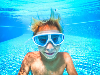 Naklejka premium Underwater view of a young boy having fun into the swimming pool. Happy teenager smiling with scuba mask. Tourist enjoying summer holiday playing in the water. Youth, vacation happiness concept