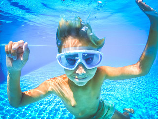 Underwater view of a young boy having fun into the swimming pool. Happy teenager with scuba mask. Tourist teen enjoying summer holiday playing in the water. Youth, summer vacation happiness concept