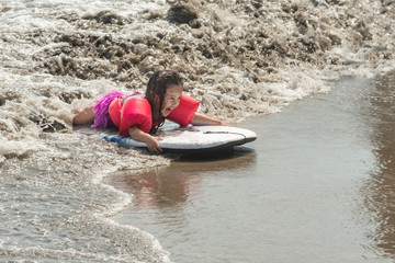 Fototapeta na wymiar Little child surfing the sea waves. Girl, riding waved filled with joy