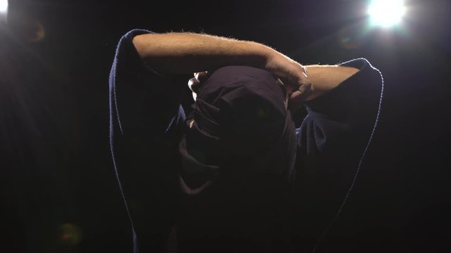 Close-up of kendo warrior is putting on helmet at background spotlights. Dolly shot