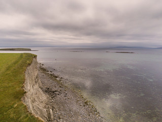 Wave breaker and pier, Spiddal, county Galway, Ireland, Burren in the background. Cloudy sky, Atlantic ocean.