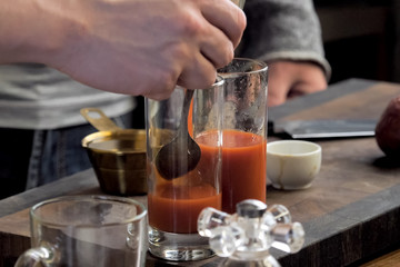 Pouring tomato juice into glasses through spoon.