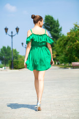 Young beautiful brunette girl in green dress walks along the embankment of the river Volga in Samara