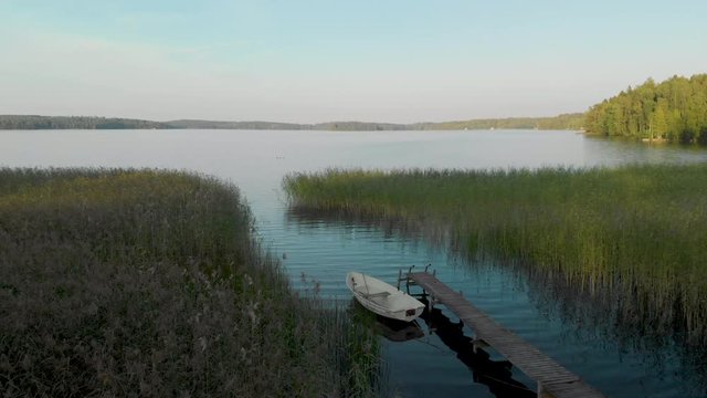 Aerial, static, drone shot, of a rowboat, at a wharf, surrounded by reed, in calm waters of lake Hvittrask, on a sunny, summer day, in Kirkkonummi, Uusimaa, Finland
