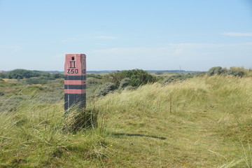 A beacon in the dunes with a lighthouse on the horizon on Ameland