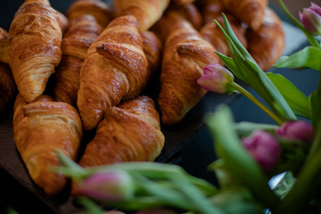 Hot croissants and pink tulips on the black table
