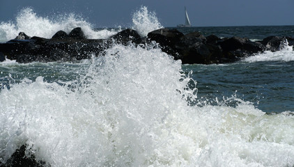 Obraz premium Two waves can be seen in the foreground and background while a sail boat goes by.