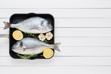 Two raw sea bream fish (dorado) in a pan on the white wooden table. Top view, copy space. Mediterranean seafood concept