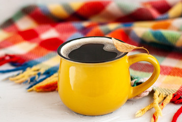 Bright yellow cup with a hot coffee drink, on a cup a dry autumn orange leaf on a white background with a bright plaid.