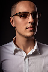 Fototapeta premium Style elegant young business man in eye glasses looking sreious and arrogant on dark shadow background. Closeup