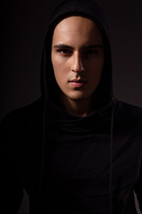 Mysterious angry man in black hoodie with hood on the head on dark background. Dangerous criminal person