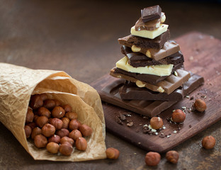 The different grades of chocolate put by the hill on a wooden board, with a filbert in a paper package on a rusty metal surface. 