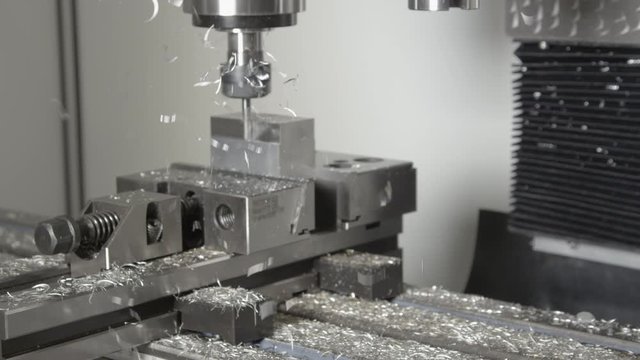 SLOW MOTION, CLOSE UP: Shiny chips fly off a piece of aluminium being processed by a CNC drill. Conventional fine end mill drill cutting and shaving a small block of metal into an unfinished product.