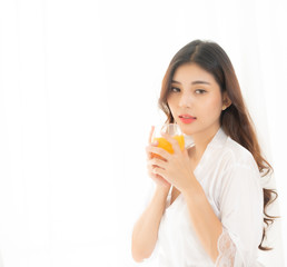 Portrait of a cute woman with brunet hair wearing white dress isolated over white background , drinking orange juice cocktail from a glass.