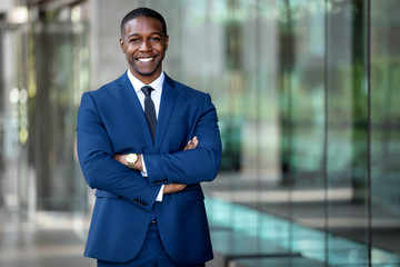 Smiling african american businessman CEO standing proud with arms crossed outside office workplace, colorful, reflective glass building, copy space - obrazy, fototapety, plakaty