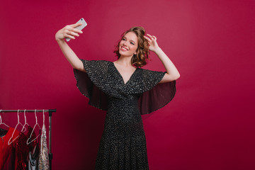Adorable female model with beautiful smile making selfie in dressing room. Indoor photo of chilling...