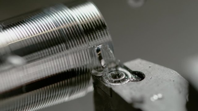 SLOW MOTION, MACRO, DOF: CNC machine spins a small workpiece while manufacturing a shiny bolt. Spiral shaped chips fly off aluminium rod being processed into a bolt. Detailed view of threading process