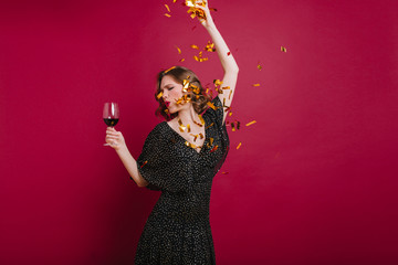 Studio shot of cheerful woman dancing at party and holding wineglass. Indoor portrait of funny...