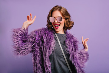 Stunning cute girl with curly brown hair posing with pleasure on purple background. Indoor photo of...