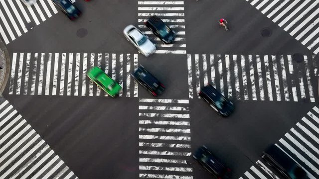 4K Timelapse high angle aerial view zoom out wide shot of pedestrian man and woman walking crossing the street crosswalk with traffic driving cars on the road in summer at Ginza, Tokyo, Japan.