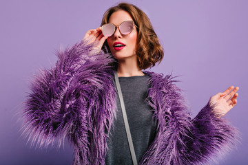 Indoor portrait of stylish european female model in glasses posing on purple background. Photo of...