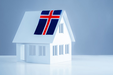 Cottage with white walls and the flag of Iceland. Immigration to Iceland. Moving to another country. Accommodation in Reykjavik. Miniature house with a flag on the roof.
